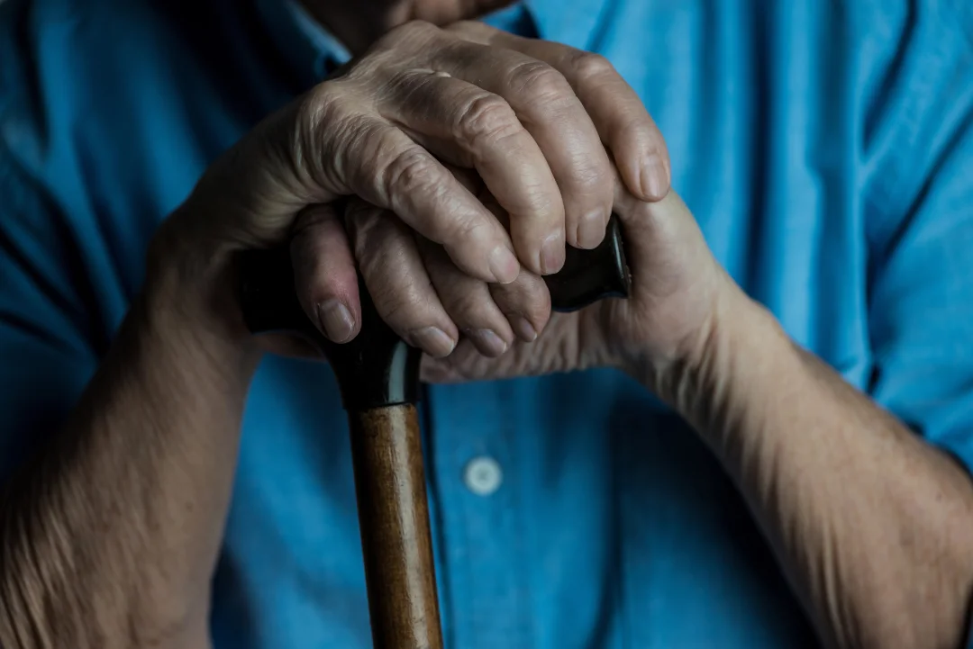 Older person's hands clasped around a walking cane